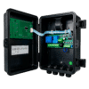 Open electrical control enclosure exposing green PCB, ribbon cable, and green terminal board inside a black housing, showing wiring and connectors for an electrical control system.