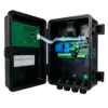 Open electrical control enclosure exposing green PCB, ribbon cable, and green terminal board inside a black housing, showing wiring and connectors for an electrical control system.